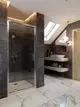 Duschbereich mit modernem Design, ausgestattet mit einer von Ideal Standard stammenden Brausearmatur. Sichtbare Glastür und große Steinfliesen. Badezimmer mit hölzernem Regal.
